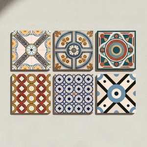Op de afbeelding: Een set van zes vierkante decoratieve tegels, gerangschikt in twee rijen van drie. Elke tegel heeft een eigen geometrisch of bloemmotief in diverse kleuren, waaronder blauw, rood, geel, zwart en crème. De ontwerpen bevatten cirkelvormige motieven, kruispatronen en rasterachtige indelingen met symmetrische vormen.