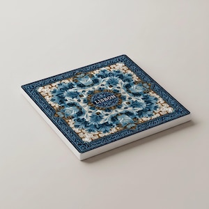 K&ouml;nnte beinhalten: Quadratischer Keramikuntersetzer mit detailliertem blau-wei&szlig;em Blumendesign. Der Untersetzer hat einen dunkelblauen Rand und tr&auml;gt das Wort "LISBON" in einem kreisf&ouml;rmigen Emblem. Das Design erinnert an traditionelle Fliesenarbeiten.