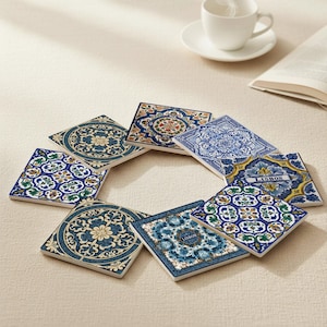 May include: A set of square ceramic coasters with detailed blue, white, and yellow floral and geometric designs. Some coasters display the word "LISBON". The coasters are arranged in a circular pattern on a beige surface.
