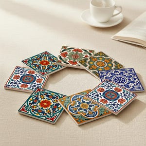 May include: A collection of eight square ceramic coasters with colorful floral patterns. The coasters feature a variety of designs in shades of red, blue, green, and yellow. A white teacup and saucer are in the background.