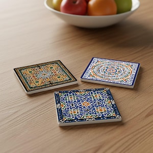 May include: Three square ceramic coasters with intricate, colorful patterns. One has a blue border and a design with orange, white, and blue elements. Another features a black border with a yellow and green design. The third has a blue and orange design.