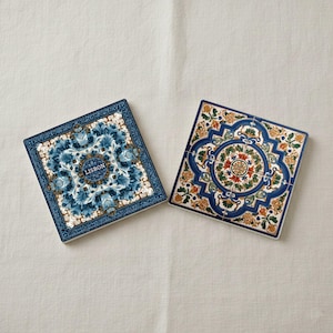 K&ouml;nnte beinhalten: Zwei quadratische Keramikuntersetzer mit aufwendigen Blumenmustern. Einer zeigt ein blau-wei&szlig;es Muster mit dem Wort "LISBON". Der andere hat einen blauen Rand mit orangefarbenen, gr&uuml;nen und wei&szlig;en Blumenmotiven. Auf neutralem Hintergrund.