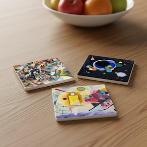 May include: Three square ceramic coasters with abstract art designs. One coaster features a colorful, swirling pattern, another has a black background with colorful circles, and the third has a geometric design with yellow and purple hues.