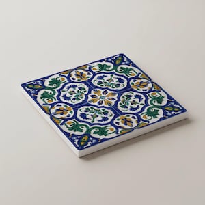 K&ouml;nnte beinhalten: Quadratische Keramikfliese mit einem sich wiederholenden Blumenmuster in Blau, Gr&uuml;n, Gelb und Wei&szlig;. Die Fliese hat einen wei&szlig;en Rand und ein detailliertes, symmetrisches Design, ideal f&uuml;r Heimdekoration oder Bastelprojekte.