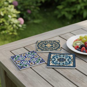 K&ouml;nnte beinhalten: Drei dekorative Keramikuntersetzer mit aufwendigen Mustern liegen auf einem Holztisch. Einer ist quadratisch mit blauem, gr&uuml;nem und gelbem Design. Ein weiterer ist rechteckig mit blau-goldenen Blumenmustern. Der dritte hat ein blau-wei&szlig;es Design mit dem Wort "LISBON".