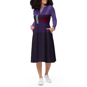 May include: A long-sleeved midi dress in shades of purple, featuring a V-neck and a color-blocked design. The dress has a dark purple skirt, a lighter purple bodice, and a teal and burgundy accent. The model is wearing white sneakers.
