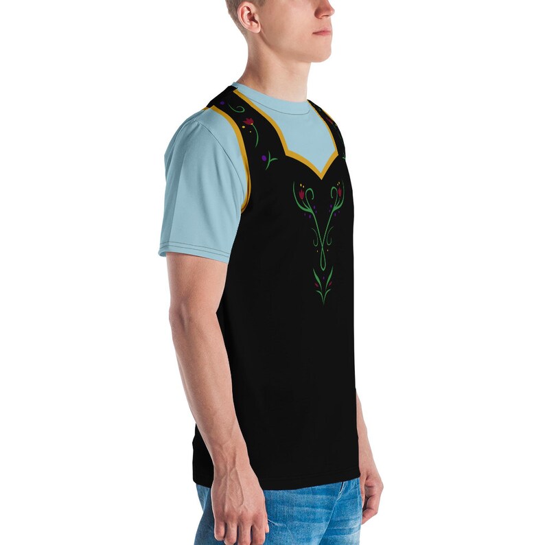 Pu&ograve; includere: Una t-shirt nera e blu con un design dorato e verde sul davanti. Il design presenta un motivo floreale stilizzato con una forma di cuore al centro.