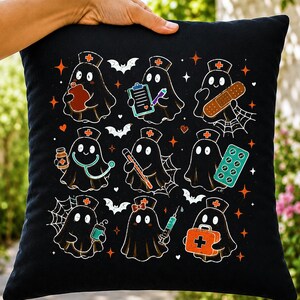 May include: A black square throw pillow featuring a repeating pattern of nine cartoon ghosts dressed as nurses. The ghosts are depicted with medical items including a clipboard, bandage, stethoscope, thermometer, pills, IV bag, syringe, and medical kit.