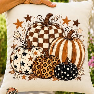 Puede incluir: Un cojín cuadrado de color blanco roto con un estampado gráfico de cuatro calabazas con varios patrones, incluyendo cuadros marrones y blancos, estrellas negras, estampado de leopardo y lunares blancos, con estrellas y hojas marrones.