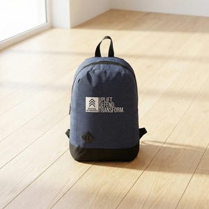 May include: A navy blue backpack with a black base and handle. The backpack features the text "UPLIFT. DEFEND. TRANSFORM." and the words "SOCIAL WORKERS" in a white square. The backpack is on a light wood floor.