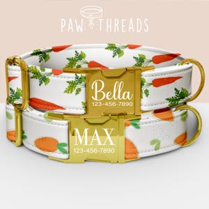 Könnte beinhalten: Zwei personalisierte Hundehalsbänder mit goldfarbener Hardware. Die Halsbänder sind weiß mit einem Karottenmuster. Eines ist mit "Bella" und einer Telefonnummer beschriftet, das andere mit "Max" und einer Telefonnummer.