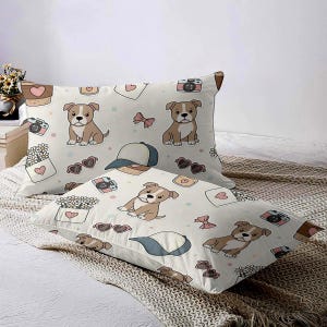 May include: Two rectangular pillowcases with a repeating pattern of brown and white puppies, cameras, sunglasses, bows, and hearts on a cream background. One pillowcase is slightly angled, showing the pattern more clearly.