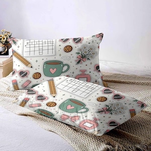 May include: Two white pillowcases with a repeating pattern of a crossword puzzle, coffee cup with a heart, heart-shaped sunglasses, pencils, cookies, perfume, and flowers. The pillowcases are on a bed with a beige blanket.