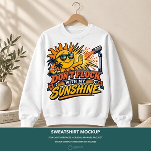 May include: A white crewneck sweatshirt featuring a graphic of a smiling sun wearing sunglasses, palm trees, and a security camera. The text reads DON'T FLOCK WITH MY SUNSHINE in orange and yellow lettering, accented by hibiscus flowers.