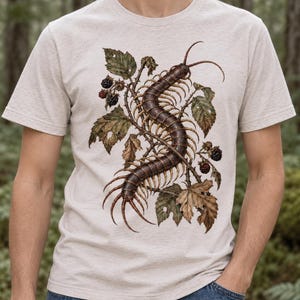 Op de afbeelding: Een gemêleerd lichtbeige t-shirt met korte mouwen en een gedetailleerde grafische illustratie van een lange bruine duizendpoot die door een tros groene en bruine braambladeren en donkerpaarse bessen op de borst kronkelt.