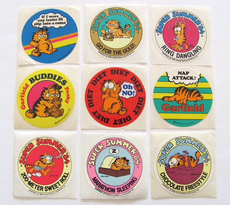 May include: Nine round stickers featuring Garfield the cat in various summer-themed poses. The stickers have a red, yellow, blue, and green background with white text. The text on the stickers includes "Super Summer '84", "Go for the Gold!", "Ring Dangling", "Nap Attack!", "Buddies", "Diet Diet Diet", "200-Meter Sweet Roll", "Marathon Sleeping", and "Chocolate Freestyle".