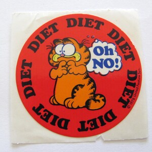 May include: A red circular sticker with the words "Diet" repeated around the edge. In the center is a cartoon orange cat with a thought bubble that says "Oh No!"  The text at the bottom reads "&copy; 1978 United Feature Syn."