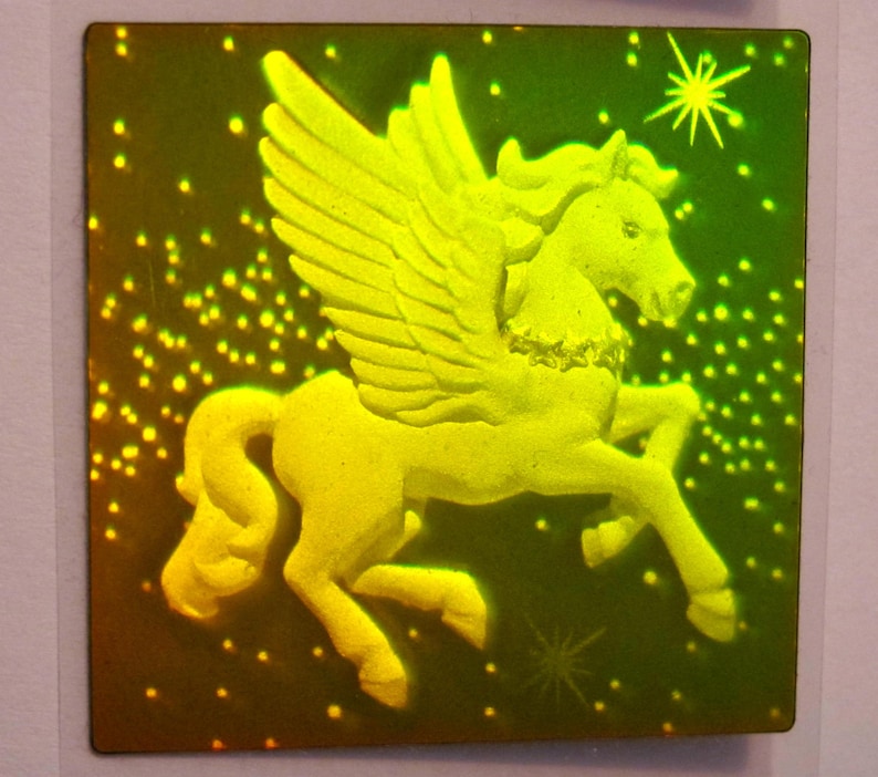 Puede incluir: Un Pegaso de color dorado con las alas extendidas, sobre un fondo verde oscuro con una dispersi&oacute;n de puntos blancos. El Pegaso est&aacute; en una pose de vuelo con la cabeza girada hacia un lado.