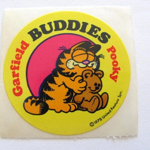 May include: A yellow circular sticker with the text "Garfield Buddies Pooky" in a black and red font. The sticker features a cartoon image of Garfield the cat hugging a brown teddy bear. The text "&copy;1978 United Feature Syn." is at the bottom of the sticker.