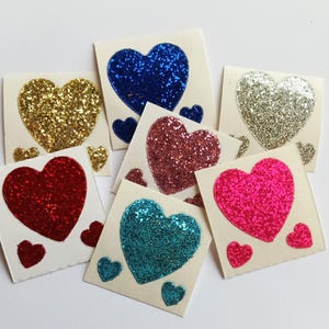 May include: Assortment of glitter heart stickers in various colors, including gold, red, blue, pink, and teal. Each sticker features a large heart with smaller hearts surrounding it.
