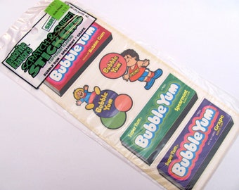 Puede incluir: Un paquete de pegatinas vintage "Scratch & Sniff" con sabores de chicle. El paquete incluye pegatinas con el texto "Bubble Yum" y personajes de dibujos animados. Las pegatinas están en una bolsa de plástico transparente.