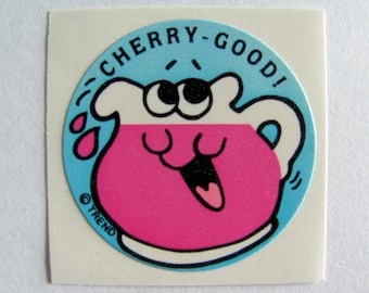 Könnte beinhalten: Ein runder Aufkleber mit blauem Hintergrund und weißem Rand. Der Aufkleber zeigt einen Cartoon-Krug mit einer rosa Flüssigkeit und einem lächelnden Gesicht. Der Text "CHERRY-GOOD!" ist in einem weißen Bogen um den Krug geschrieben. Der Text "© TREND" ist in einem weißen Bogen am unteren Rand des Aufklebers geschrieben.