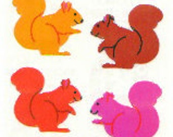 May include: Four felt squirrel shapes in orange, brown, red, and pink. The squirrels are all facing the right side of the image and have their tails curled up behind them.