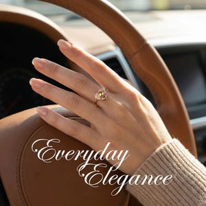 Puede incluir: Un anillo de oro con un dise&ntilde;o en forma de coraz&oacute;n, con una piedra preciosa amarilla central y piedras m&aacute;s peque&ntilde;as. El anillo est&aacute; en una mano, con el texto "Everyday Elegance" en escritura blanca.
