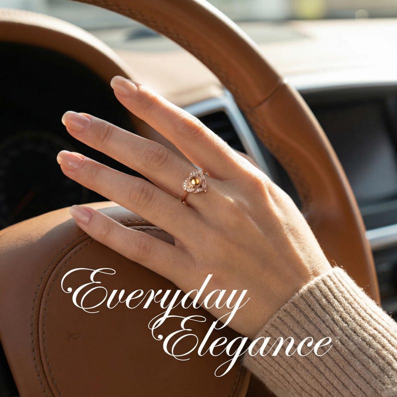 Puede incluir: Un anillo de oro con un dise&ntilde;o en forma de coraz&oacute;n, con una piedra preciosa amarilla central y piedras m&aacute;s peque&ntilde;as. El anillo est&aacute; en una mano, con el texto "Everyday Elegance" en escritura blanca.
