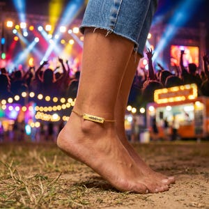 Peut inclure: Un bracelet de cheville doré avec un pendentif rectangulaire orné d'un motif d'onde sonore. Le bracelet est porté à la cheville, avec en arrière-plan une scène de concert avec une foule et des lumières.