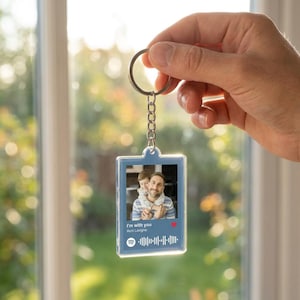 May include: A clear acrylic keyring with a silver metal ring and chain. The keyring features a photo of a man and child, with the text "I'm with you" and the artist's name. A Spotify code and a heart icon are also visible.