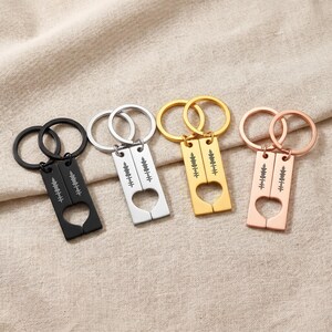 May include: Four keyrings in black, silver, gold, and rose gold. Each keyring has a rectangular tag with a heart-shaped cutout and a sound wave pattern. The keyrings are silver and gold.