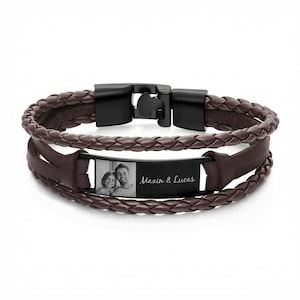 May include: A brown leather bracelet with a black clasp and a rectangular plate. The plate features a black and white photo of a couple and the text "Maxin & Lucas". The bracelet has a braided design.
