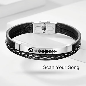 以下が含まれることがあります： 黒い革のブレスレット、ステンレス製の留め金付き。ブレスレットには、音符とスキャン可能な音楽コードが付いたシルバープレートが付いています。「Scan Your Song」というテキストが下にあります。