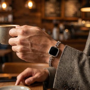 May include: A silver bracelet with a black, octagonal centerpiece. The bracelet has a chain link design and is worn on a wrist. The person is wearing a gray blazer and holding a cup of coffee.