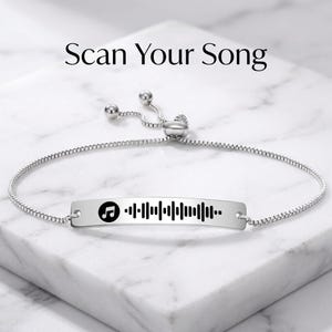 Könnte beinhalten: Silberfarbenes Armband mit rechteckigem Anhänger, der eine Musiknoten-Ikone und ein barcodeähnliches Design zeigt. Der Text "Scan Your Song" steht über dem Armband. Das Armband hat eine verstellbare Kette.