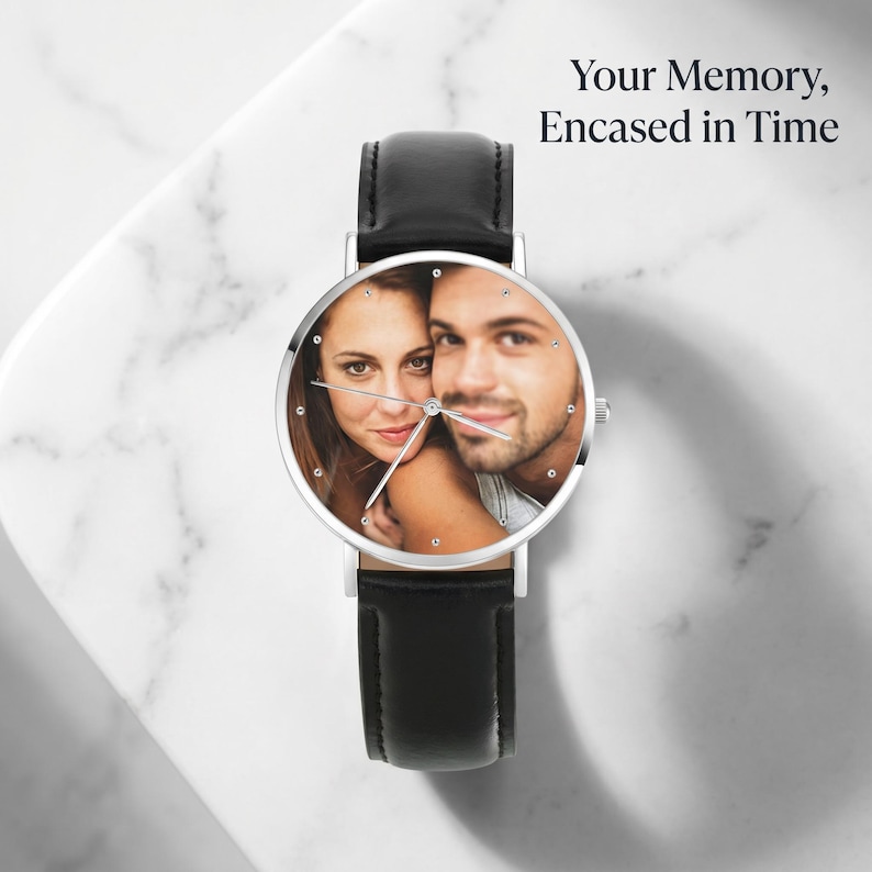 Peut inclure: Une montre-bracelet avec un bracelet en cuir noir et un bo&icirc;tier circulaire argent&eacute;. Le cadran de la montre pr&eacute;sente une photographie personnalis&eacute;e d'une femme et d'un homme. Le texte 'Your Memory, Encased in Time' est imprim&eacute; en haut &agrave; droite.