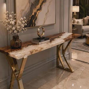May include: A rectangular console table featuring a live-edge wood top with a central white resin river inlay, supported by gold-toned metal legs. A dark glass vase with white flowers and a circular sculpture on books sit on the table surface.