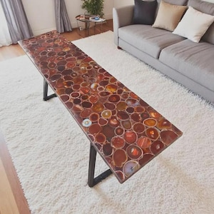 May include: A rectangular coffee table with a mosaic top made of polished agate slices in shades of red, orange, and brown. The table has a black metal frame and is set on a white rug.