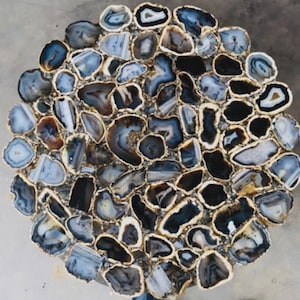 Könnte beinhalten: Runde Tischplatte Mosaik aus polierten Achatsteinen in Blau-, Grau- und Schwarztönen. Die Steine sind kreisförmig angeordnet und mit einer goldfarbenen Umrandung versehen. Die Tischplatte hat ein natürliches, organisches Aussehen.