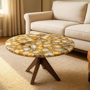 Puede incluir: Una mesa de centro redonda con una encimera única de piedra de ágata. La mesa tiene una base de tres patas de color marrón oscuro. La encimera de ágata presenta un mosaico de piedras amarillas, marrones y blancas. La mesa está sobre una alfombra beige.