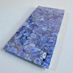 May include: A rectangular slab with a mosaic pattern of blue and purple stones. The stones are irregularly shaped and set against a dark background, creating a textured surface. The overall color palette is cool, with variations in the blue hues.