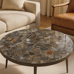 May include: Circular coffee table featuring a mosaic stone surface in grey, brown, and orange hues. The table has a dark brown metal frame and three legs. The table is a decorative piece for a living room, approximately 100 cm in diameter.
