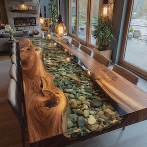 May include: A long dining table featuring two thick, natural-edge wood slabs separated by a central glass-topped channel filled with smooth, multi-colored river stones. The table is surrounded by several upholstered chairs in a dining room.