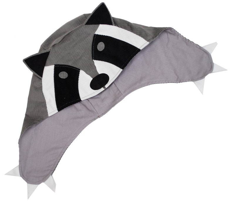 May include: Gray raccoon-shaped hooded hat with white and black details. The hood has a gray corduroy exterior and a soft gray lining.