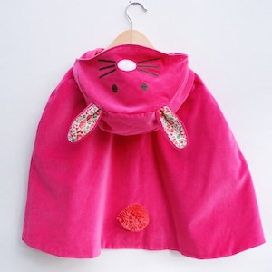 May include: A pink hooded cape with bunny ears and a pom-pom tail. The ears are lined with a floral fabric.