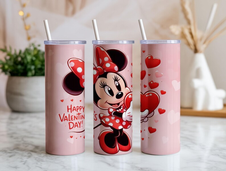 Op de afbeelding: Drie roze ge&iuml;soleerde bekers met witte rietjes. E&eacute;n beker toont Minnie Mouse met een hart, een andere zegt "Happy Valentine's Day!" met harten, en de derde heeft zwevende harten. De bekers zijn voor Valentijnsdag.