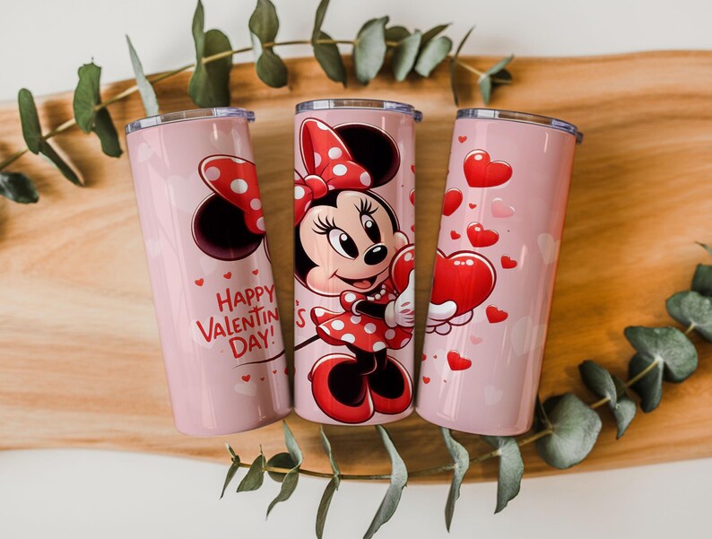 Op de afbeelding: Drie roze ge&iuml;soleerde bekers met Valentijnsdagontwerpen. E&eacute;n heeft Minnie Mouse in een rode polkadotjurk en strik, met een hart. Een andere heeft de tekst "Happy Valentine's Day!" en harten.