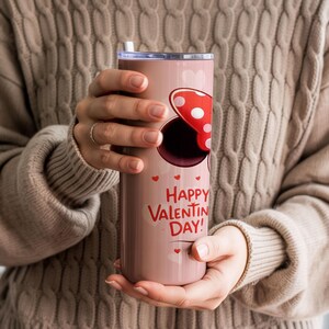 Op de afbeelding: Een roze ge&iuml;soleerde beker met een rood-wit stippen strik ontwerp en de woorden "Happy Valentine's Day!" in het rood. De beker heeft een zilveren deksel en een wit rietje.