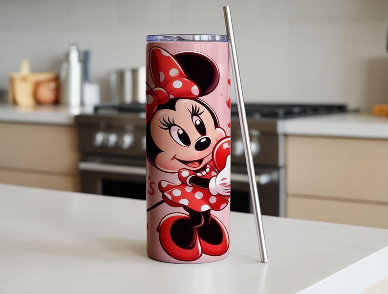 Op de afbeelding: Een roze beker met een Minnie Mouse-illustratie. Minnie draagt haar iconische rode jurk met witte stippen en een strik. Een roestvrijstalen rietje staat naast de beker. De beker is ontworpen voor koude dranken.